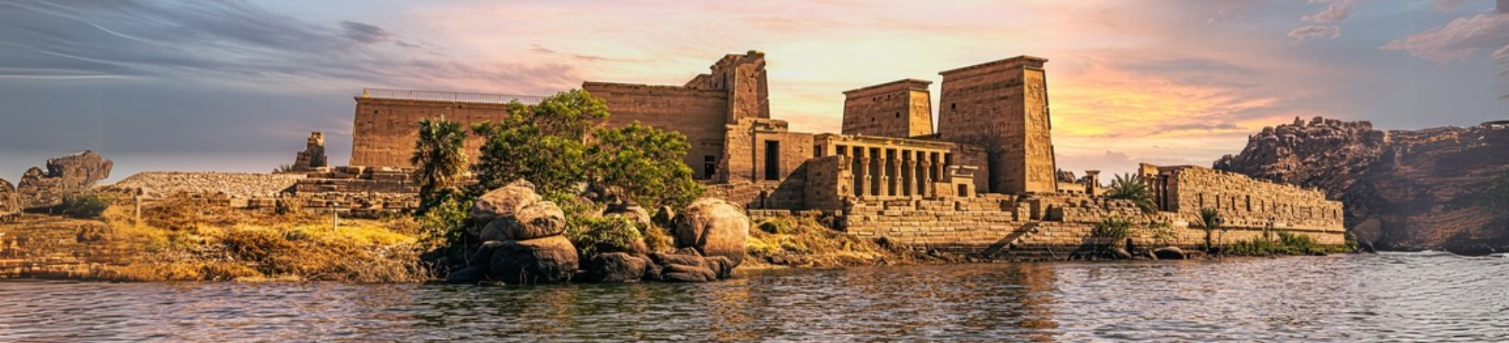 A scenic view of Philae Temple on the Nile River, illuminated by the golden light of sunset.
